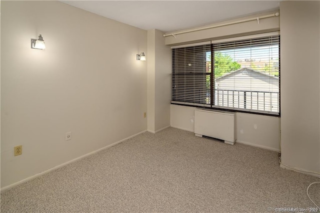 carpeted spare room featuring radiator and baseboards