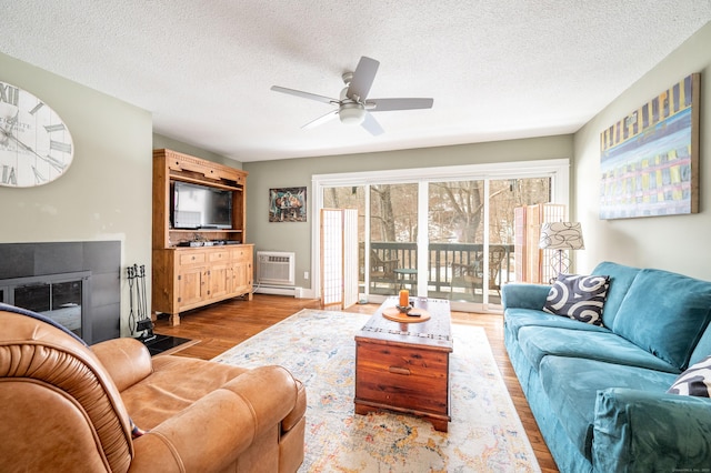 living area with a fireplace, an AC wall unit, ceiling fan, a textured ceiling, and light wood-type flooring