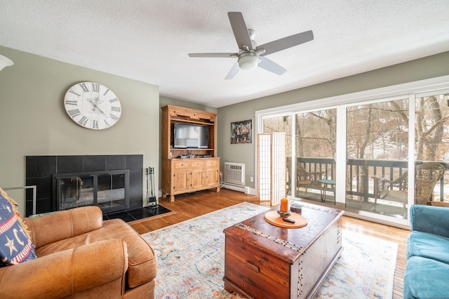 living area with a textured ceiling, a tiled fireplace, and wood finished floors