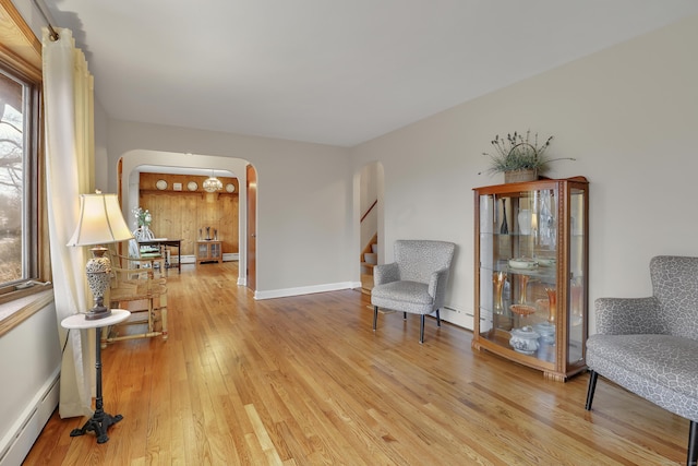 sitting room featuring arched walkways, a baseboard heating unit, baseboards, stairway, and wood-type flooring