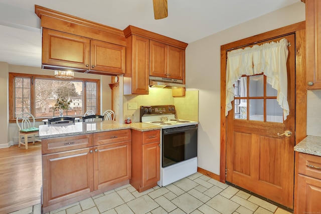 kitchen with light stone counters, white electric range, decorative backsplash, brown cabinetry, and under cabinet range hood