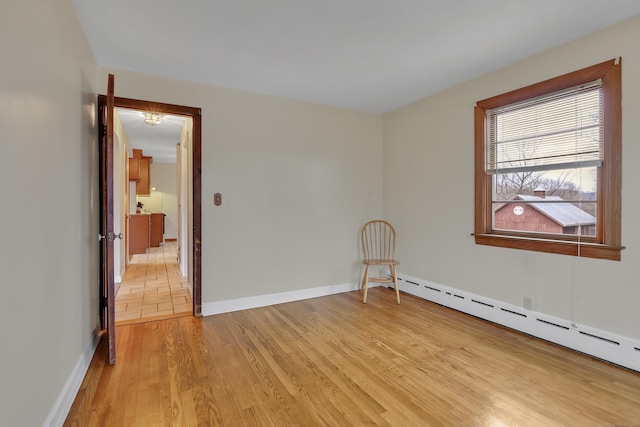 spare room with light wood-style floors, a baseboard radiator, and baseboards