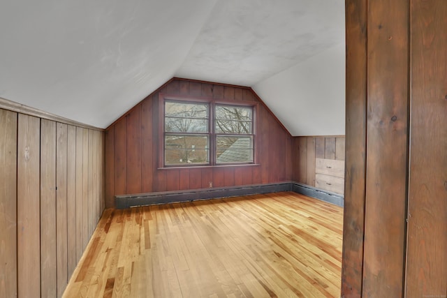 bonus room with vaulted ceiling, light wood finished floors, baseboard heating, and wooden walls