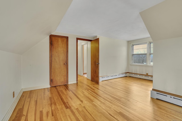 additional living space with a baseboard heating unit, vaulted ceiling, light wood-style flooring, and baseboards