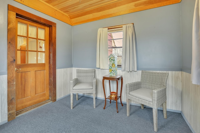 living area with carpet, wood ceiling, and a wainscoted wall