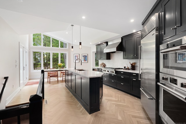 kitchen featuring light countertops, vaulted ceiling, a sink, dark cabinets, and wall chimney exhaust hood