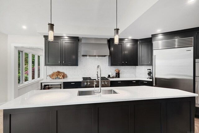 kitchen featuring a sink, wall chimney exhaust hood, tasteful backsplash, and dark cabinetry