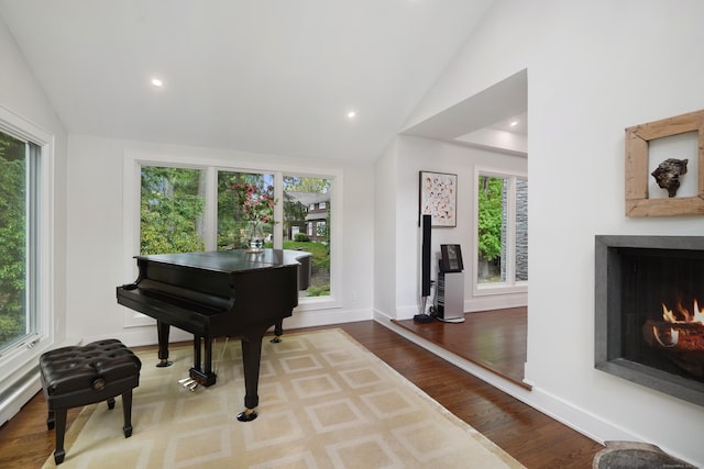 sitting room with a healthy amount of sunlight, vaulted ceiling, a lit fireplace, and wood finished floors