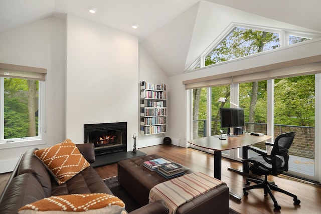 home office with a warm lit fireplace, high vaulted ceiling, and wood finished floors