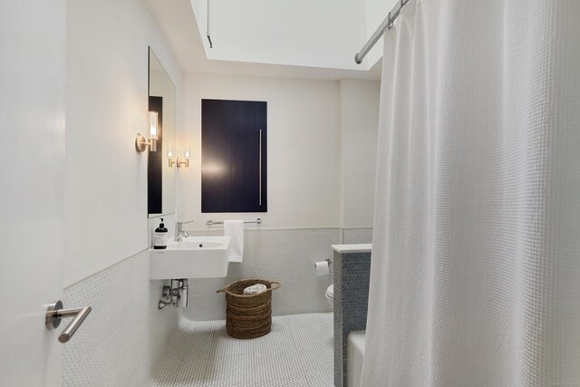 bathroom with toilet, a shower with shower curtain, a sink, tile walls, and wainscoting