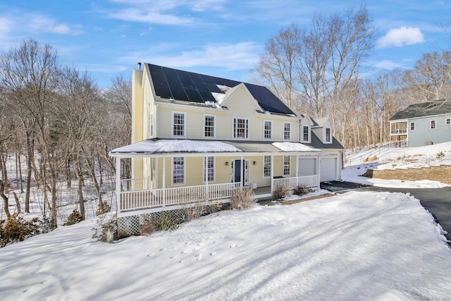 view of front of home featuring driveway, a chimney, an attached garage, covered porch, and roof mounted solar panels