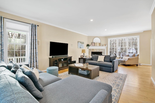 living room featuring light wood-style flooring, recessed lighting, a fireplace, baseboards, and crown molding