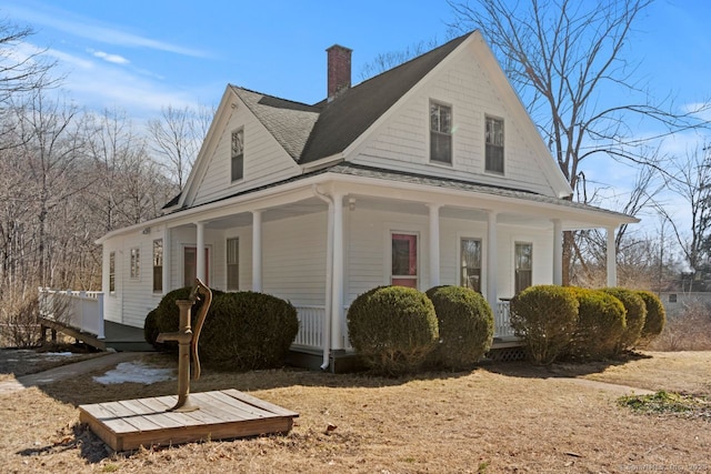 view of side of property featuring covered porch, a shingled roof, and a chimney