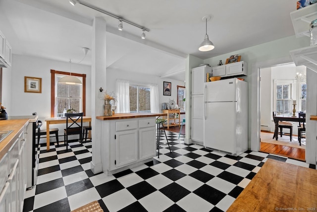 kitchen with white cabinets, butcher block countertops, freestanding refrigerator, light floors, and pendant lighting