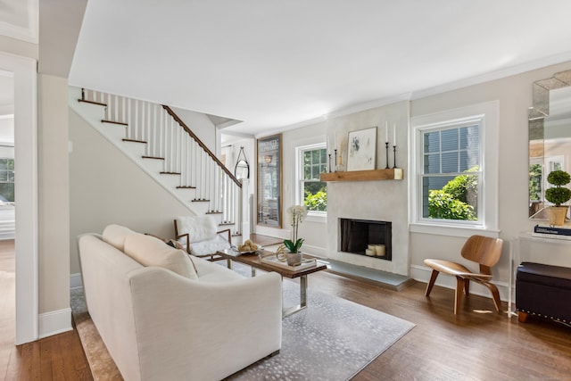 living room featuring a fireplace with raised hearth, stairway, wood finished floors, and a healthy amount of sunlight