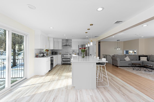 kitchen featuring light countertops, visible vents, appliances with stainless steel finishes, white cabinetry, and wall chimney range hood