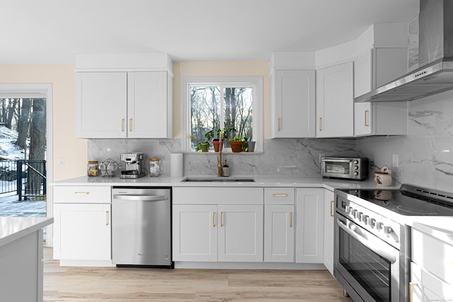 kitchen featuring stainless steel appliances, a sink, white cabinets, light countertops, and wall chimney exhaust hood