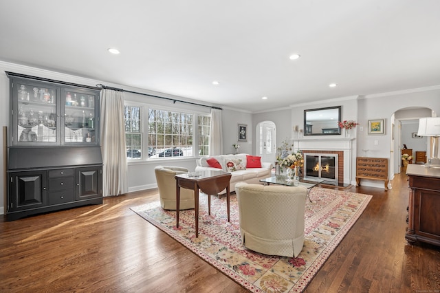 living room with arched walkways, recessed lighting, ornamental molding, dark wood-style floors, and a glass covered fireplace