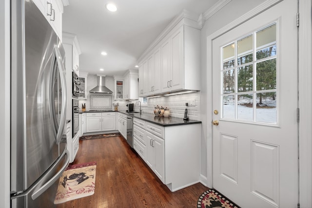 kitchen with white cabinets, dark countertops, wall chimney exhaust hood, stainless steel appliances, and a sink