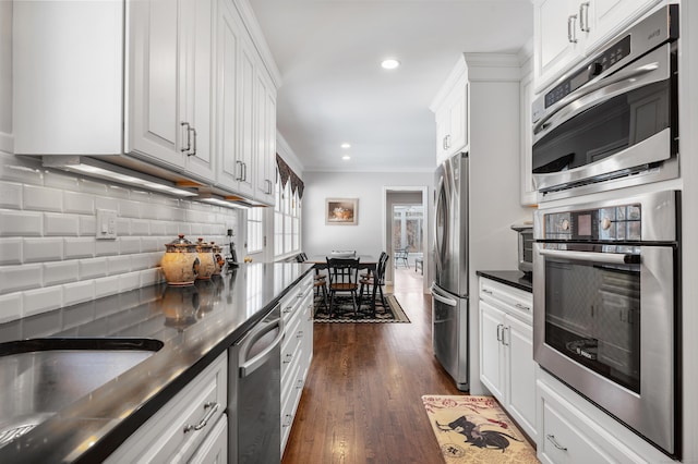 kitchen featuring stainless steel appliances, dark countertops, white cabinets, and ornamental molding