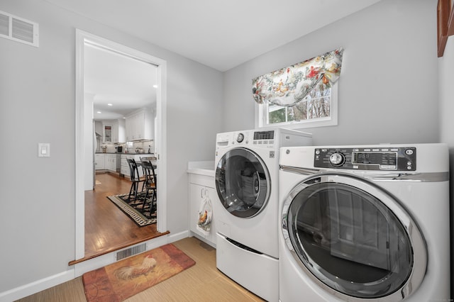 laundry area featuring cabinet space, visible vents, washer and clothes dryer, and light wood-style floors