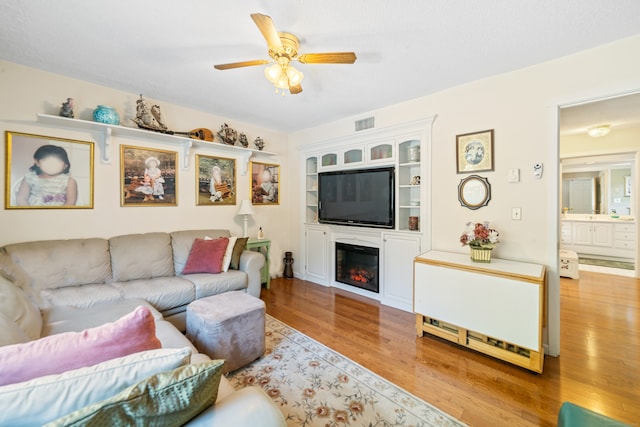 living room featuring ceiling fan, a glass covered fireplace, wood finished floors, and visible vents