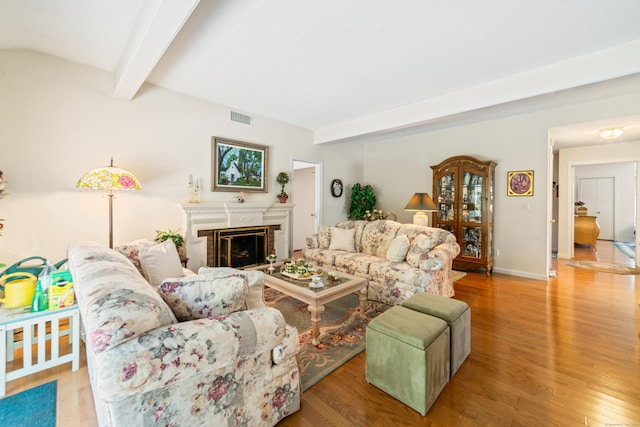 living room with beamed ceiling, a brick fireplace, wood finished floors, and visible vents