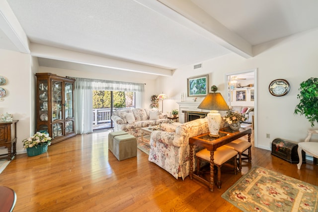 living room featuring a fireplace, beam ceiling, visible vents, and hardwood / wood-style floors