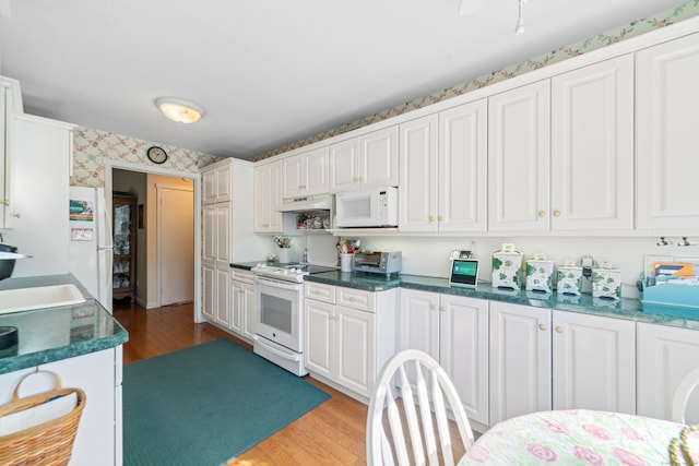 kitchen featuring a sink, wallpapered walls, white appliances, light wood-type flooring, and under cabinet range hood