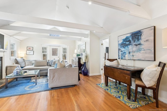 living room featuring vaulted ceiling with beams, light wood-type flooring, a glass covered fireplace, and baseboards