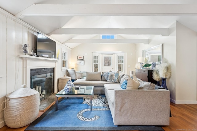 living room featuring baseboards, visible vents, a glass covered fireplace, lofted ceiling with beams, and wood finished floors