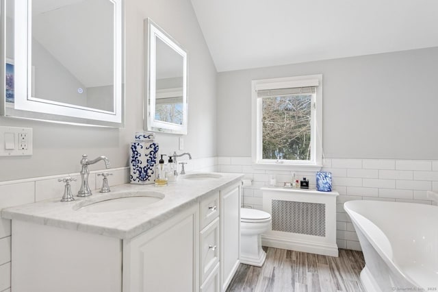 bathroom featuring toilet, a soaking tub, a sink, and wood finished floors