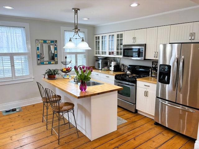 kitchen featuring white cabinets, stainless steel appliances, wooden counters, and a kitchen breakfast bar