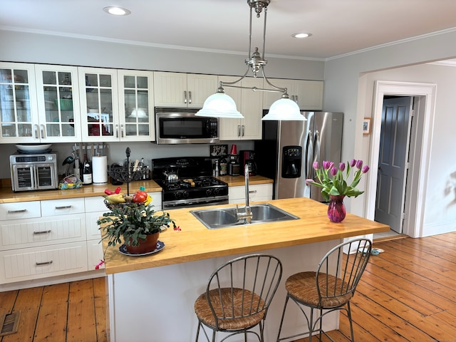 kitchen with a sink, stainless steel appliances, wood counters, and white cabinets