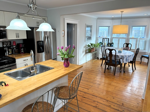 kitchen featuring a sink, wooden counters, ornamental molding, appliances with stainless steel finishes, and a wealth of natural light