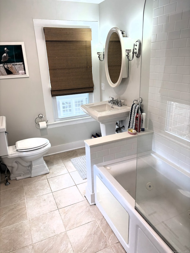 bathroom with a tub to relax in, baseboards, toilet, tile patterned flooring, and a sink