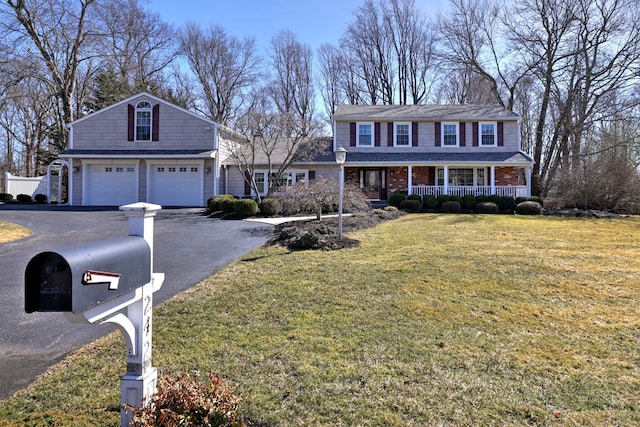 view of front of house featuring a front yard, driveway, covered porch, a garage, and brick siding