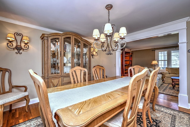 dining room featuring a notable chandelier, crown molding, baseboards, and wood finished floors