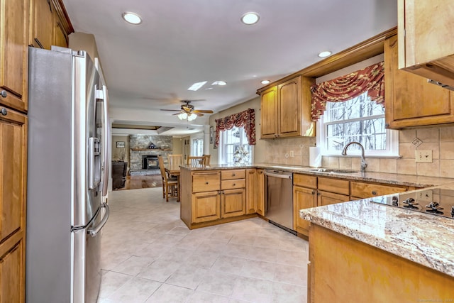 kitchen with light stone counters, a peninsula, a sink, appliances with stainless steel finishes, and open floor plan