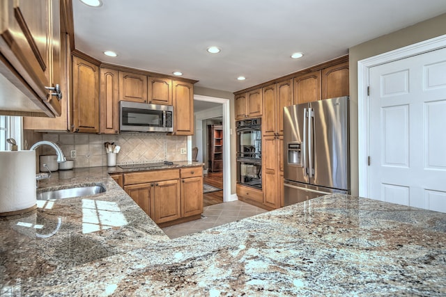 kitchen featuring light tile patterned floors, stone counters, a sink, appliances with stainless steel finishes, and tasteful backsplash