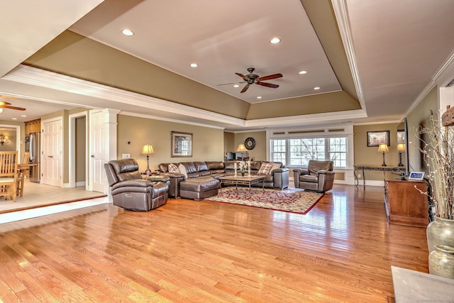 living room featuring a tray ceiling, ornamental molding, light wood-type flooring, and ceiling fan