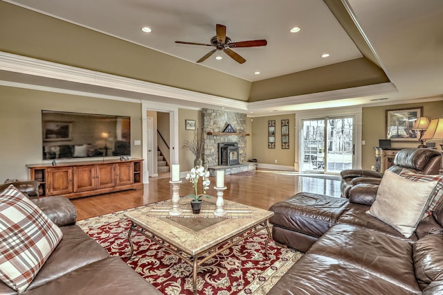 living area featuring ornamental molding, recessed lighting, light wood-style floors, a stone fireplace, and a raised ceiling