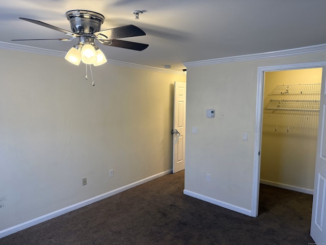 unfurnished bedroom with a walk in closet, dark carpet, ornamental molding, ceiling fan, and baseboards