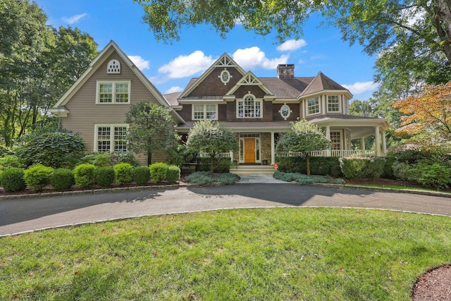 view of front facade featuring covered porch, driveway, a chimney, and a front yard