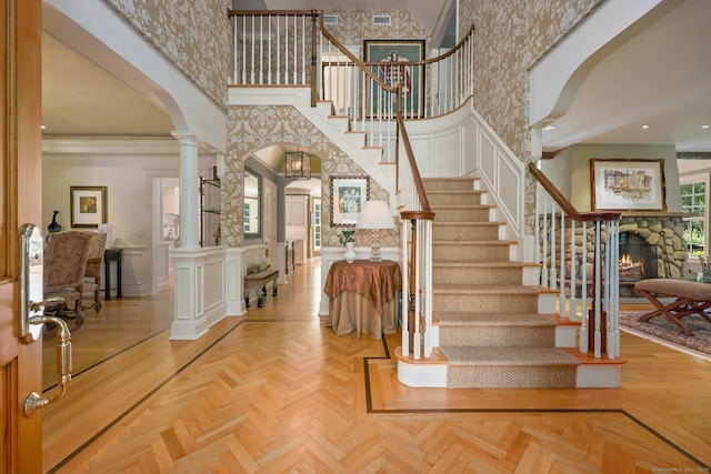 foyer entrance featuring arched walkways, a wainscoted wall, a high ceiling, ornate columns, and a decorative wall