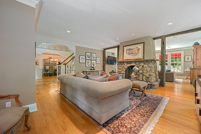 living area with arched walkways, stairway, a stone fireplace, light wood-type flooring, and a notable chandelier