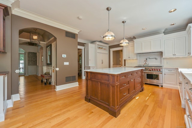 kitchen featuring arched walkways, stainless steel stove, visible vents, light countertops, and decorative light fixtures