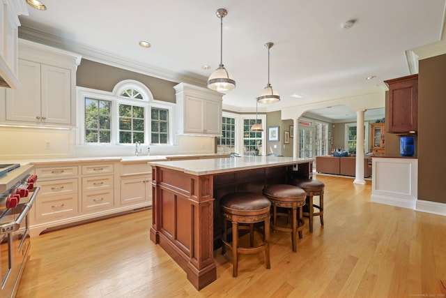 kitchen with a breakfast bar, a center island, pendant lighting, decorative columns, and light countertops