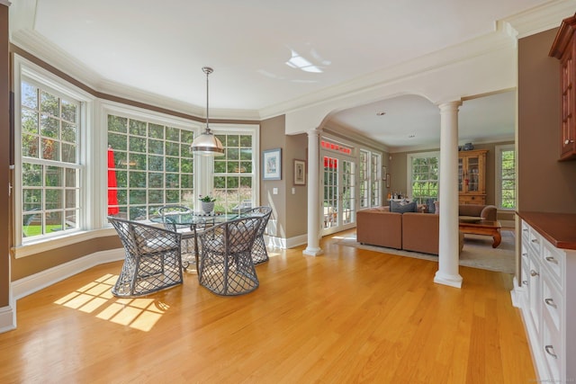 dining room with ornamental molding, light wood-type flooring, plenty of natural light, and ornate columns