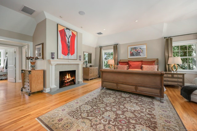 bedroom featuring a fireplace with flush hearth, visible vents, vaulted ceiling, and wood finished floors